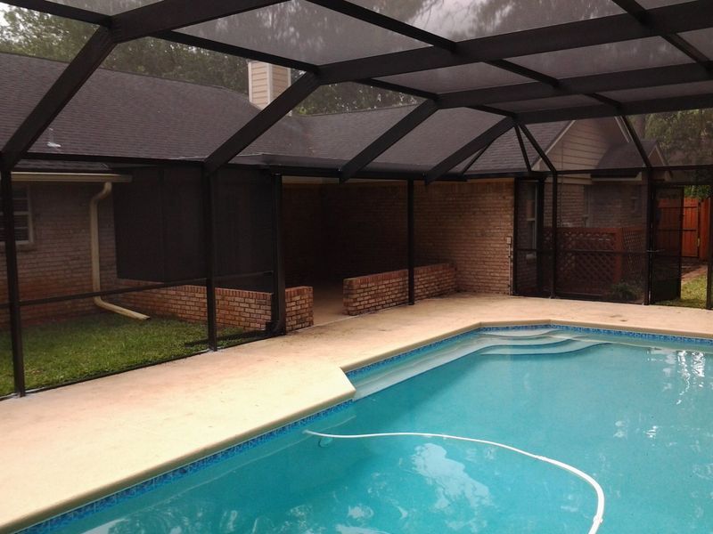 Pool area with screened enclosure. Features pool, brick walls, and a black frame.