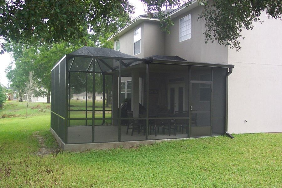 Screened-in porch attached to a two-story beige house with a dark-colored roof, surrounded by green grass.