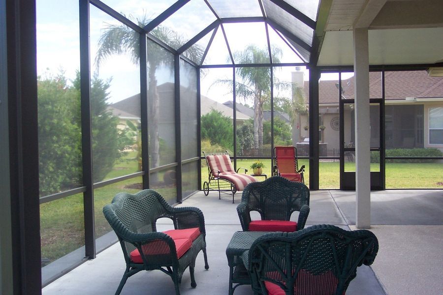 Screened-in porch with green wicker furniture, red cushions, and a view of a backyard with palm trees.