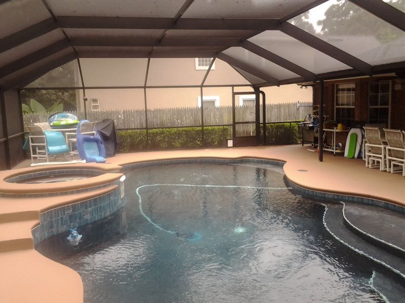 Swimming pool under a screened enclosure; adjacent hot tub, patio furniture, and house.