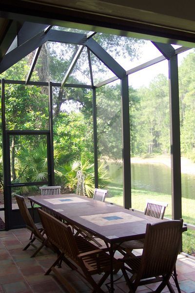 Screened-in patio with dining table and chairs, overlooking a lake and trees.