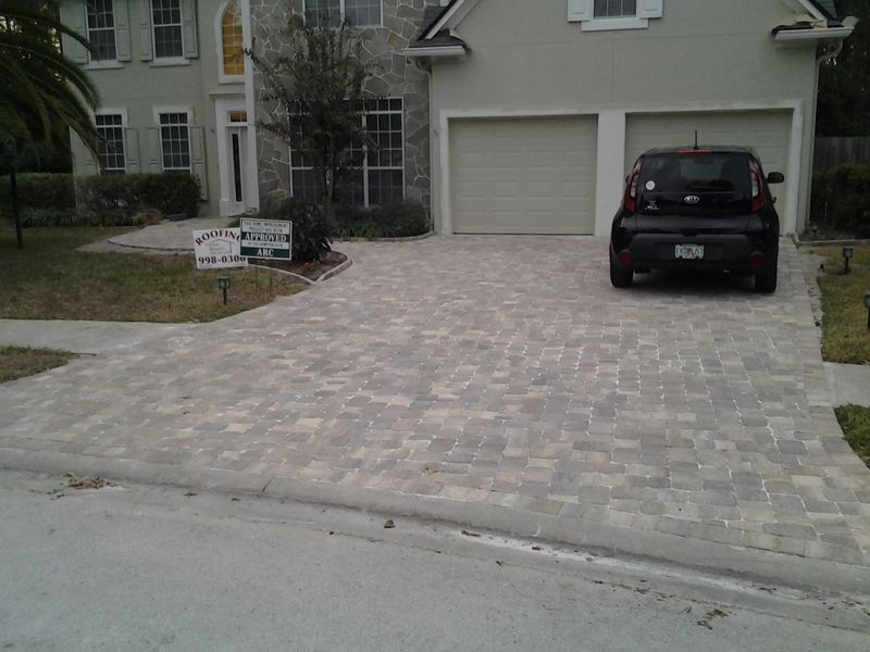 Driveway paved with gray pavers in front of a house, car parked in driveway.