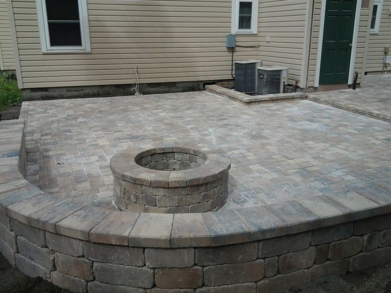 Brick patio with a built-in fire pit and retaining wall in front of a house.