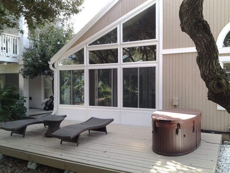 A-frame house exterior with large windows, deck with lounge chairs and a hot tub.