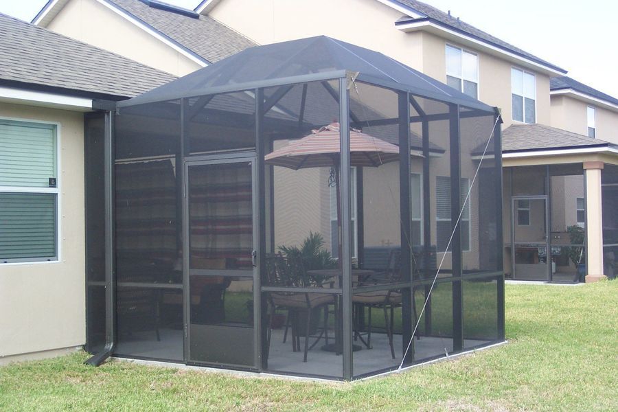 Screened-in patio enclosure attached to a house; includes a table, chairs, and an umbrella, on a concrete slab.