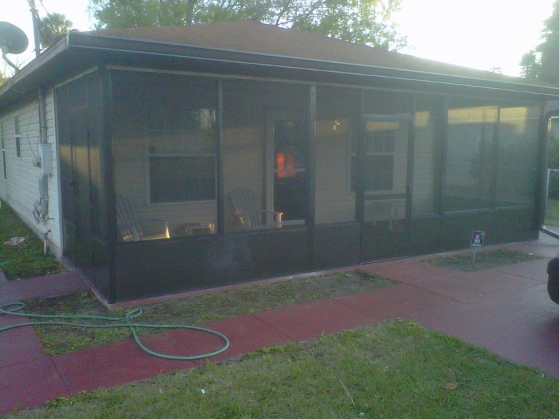 Screened-in porch attached to a white house with a brown roof and a red painted concrete patio.
