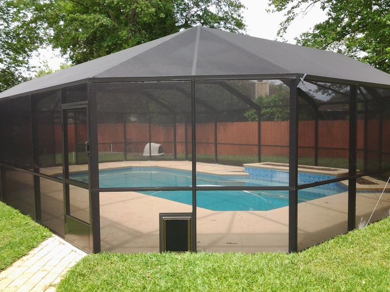 A screened-in pool enclosure with a hexagonal roof; pool with turquoise water, surrounded by concrete, and grass.
