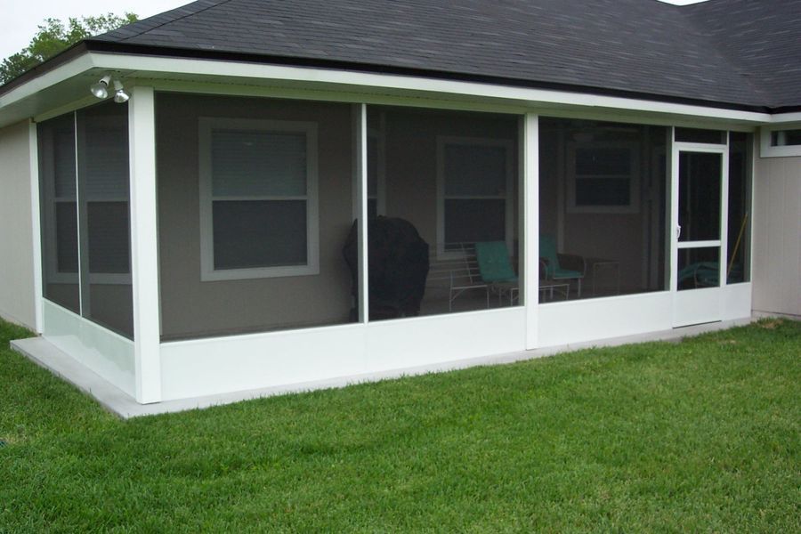 White screened-in porch attached to a house with a dark roof and green grass in the foreground.