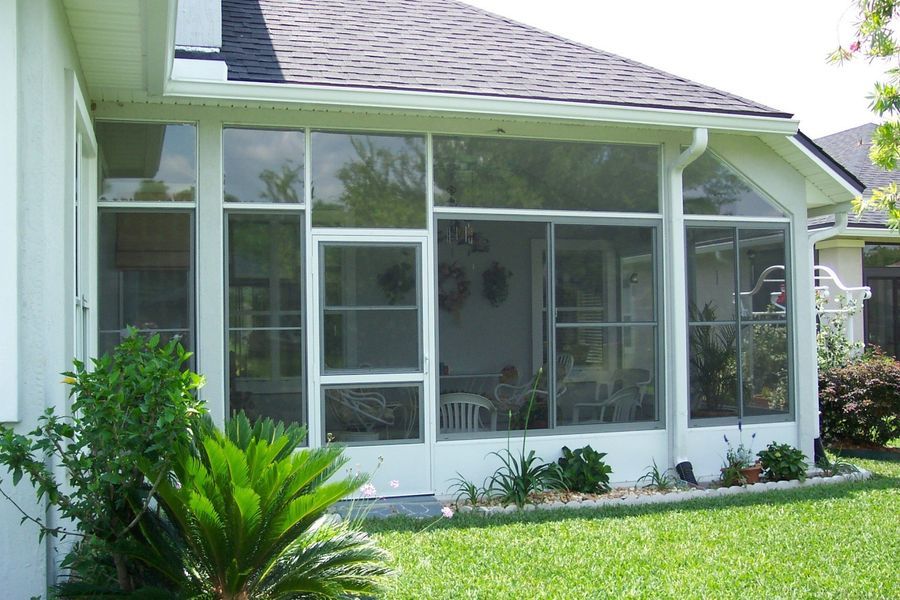 Screened-in porch with white frames, glass and screen panels, and a dark roof. Green foliage and lawn in the foreground.