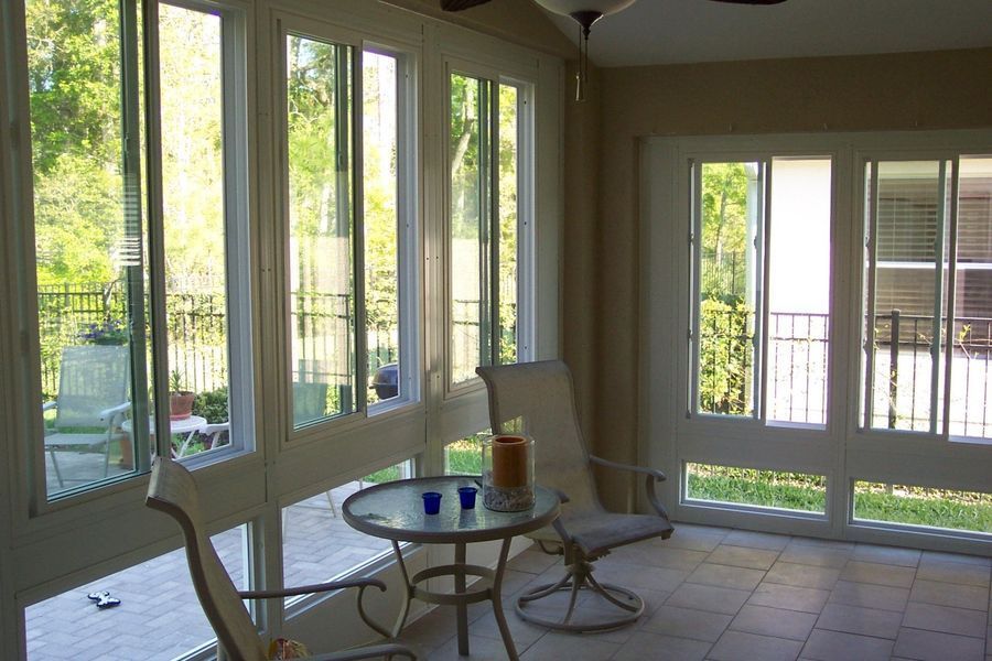 Sunroom with white-framed windows and doors, small table and chairs, overlooking a patio and greenery.