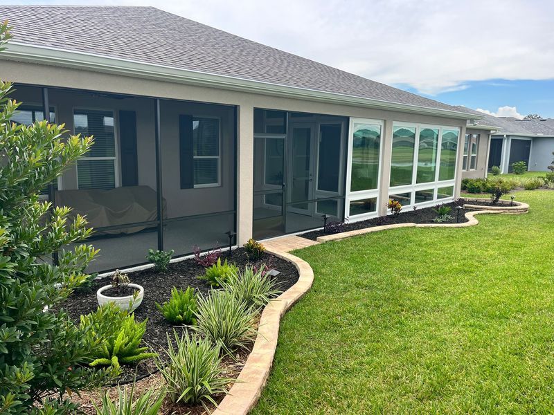 Screened-in porch on a house with a neatly landscaped yard and a gray roof.