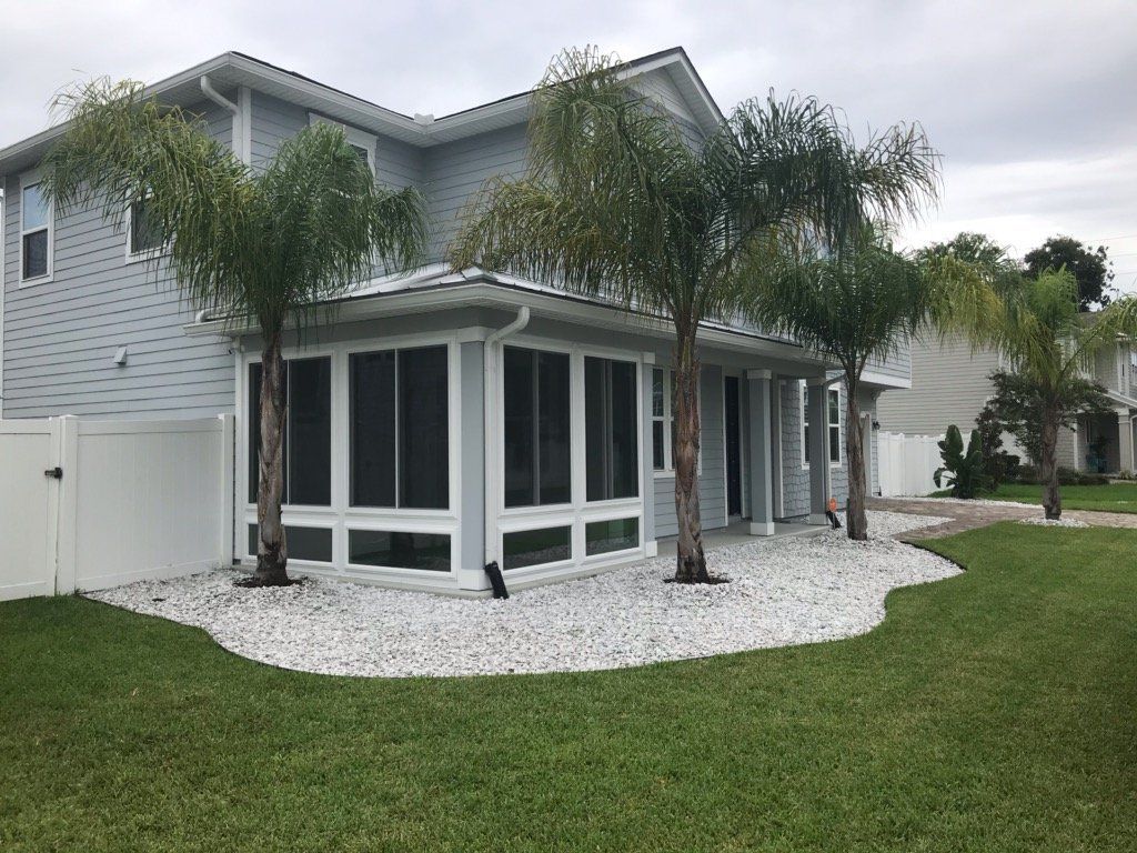 Backyard with screened porch, palm trees, white gravel bed, and green lawn.
