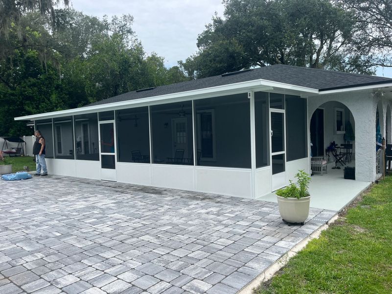 Screened-in patio with dark roof, white frame, gray screens, and brick patio. Person standing on the left.