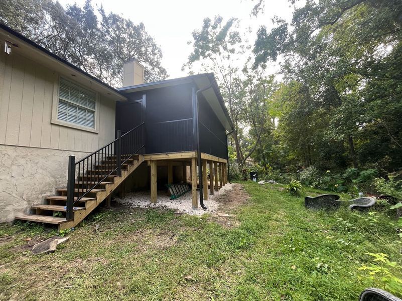 Exterior view of a house with a screened porch and wooden stairs leading down to a yard with trees.