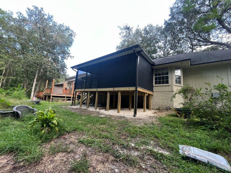 A screened porch attached to a house; dark screen, wood supports, and green yard.