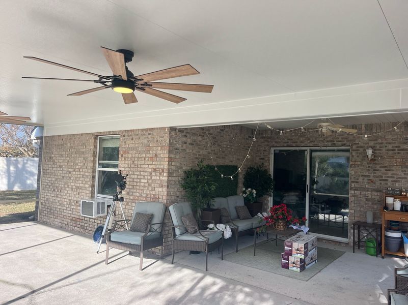 Patio with brick wall, seating, ceiling fans, and string lights.