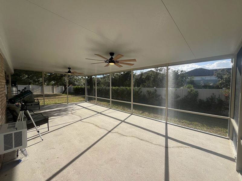 Screened patio with concrete floor, two ceiling fans, and outdoor furniture.