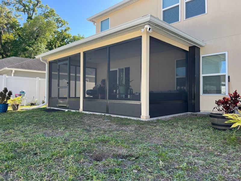Screened patio attached to a two-story beige house, overlooking a grassy backyard.