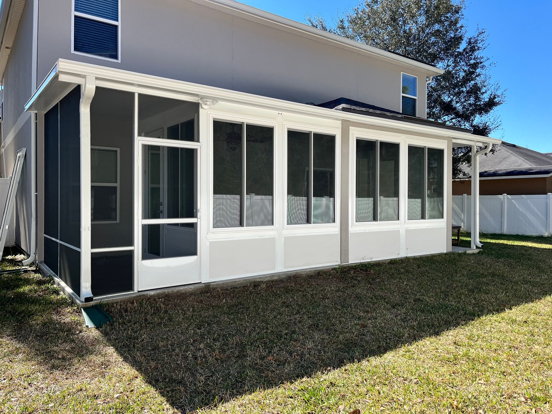 Screened-in porch attached to a two-story house with gray siding. Porch has white trim and dark screening.