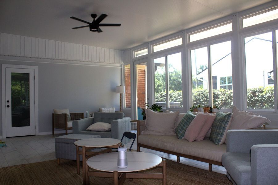 Sunroom with large windows, light gray walls, white trim, and a ceiling fan. Furnished with sofas and coffee tables.
