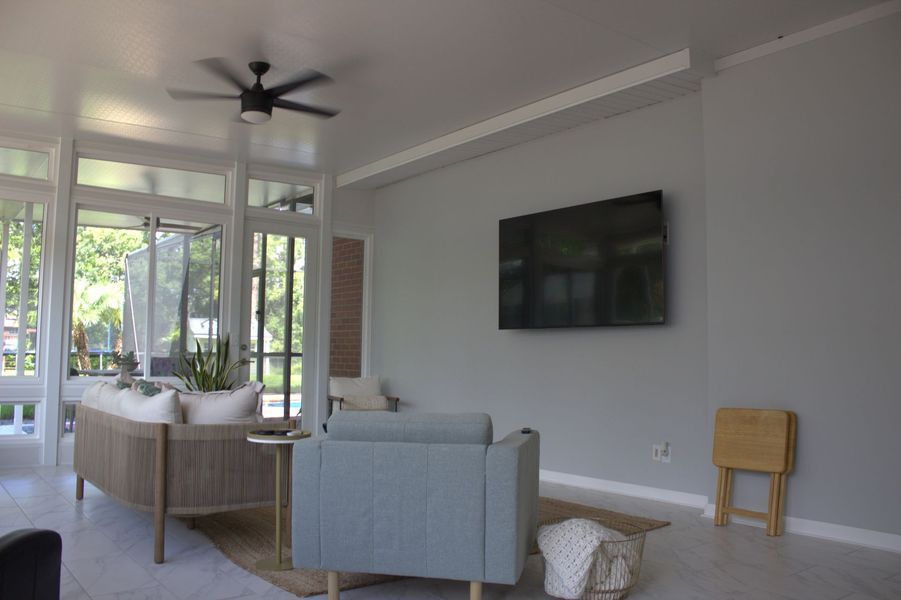 Living room with a mounted TV, light blue armchair, and a sofa near glass windows.