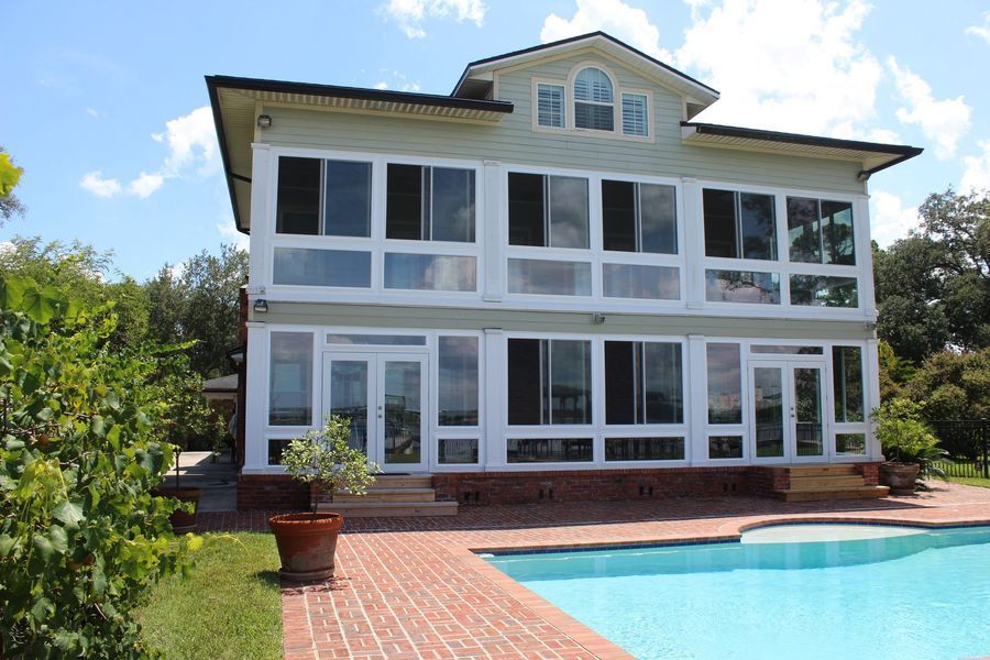 Two-story house with large windows, poolside, blue sky.