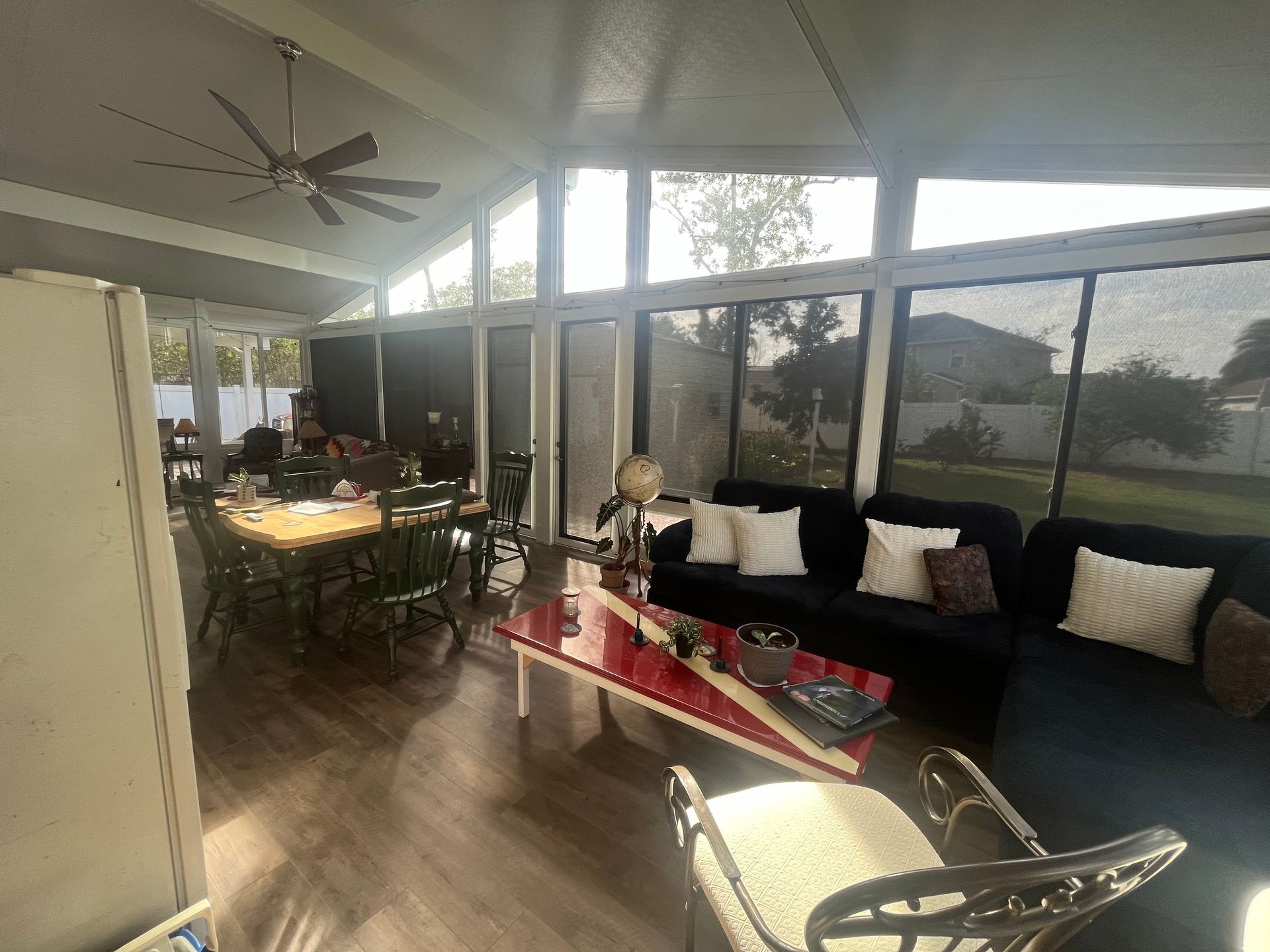 Sunroom interior with a sofa, table, and dining set. Windows look out to a yard.