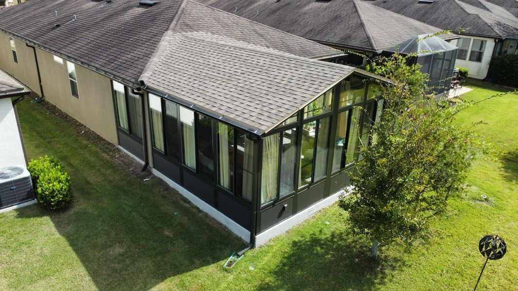 Back of a house with dark gray roof, sunroom with many windows, green lawn.
