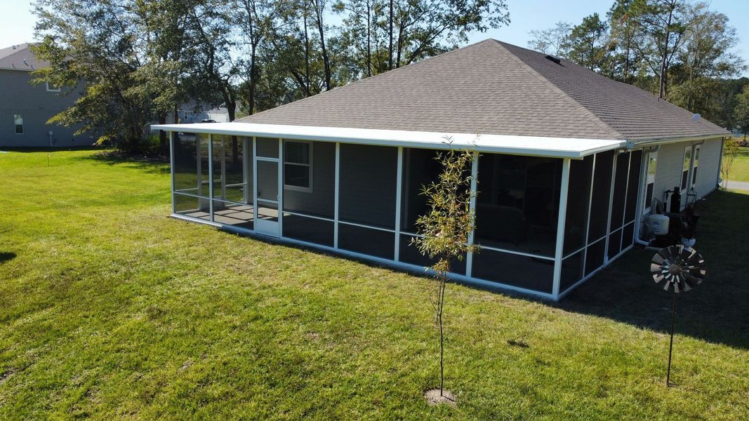 Screened-in porch on a single-story house in a grassy yard, with a small tree and windmill.