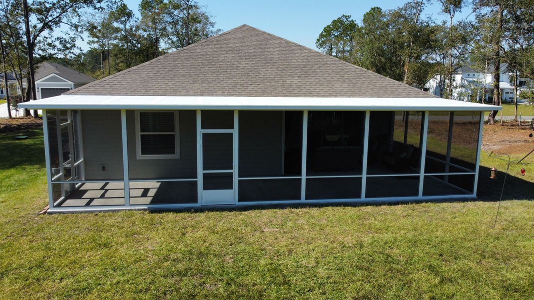 Screened-in porch on a house with white framing. The porch is surrounded by green grass under a clear, sunny sky.