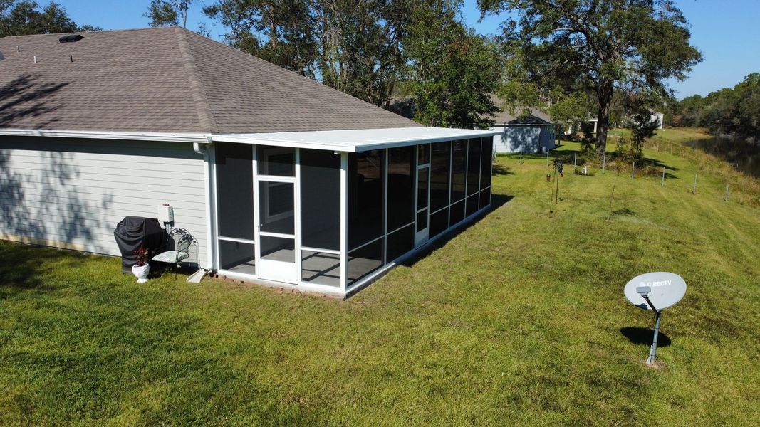Screened-in porch attached to a light gray house. Man near air conditioning unit. Satellite dish in grassy yard.