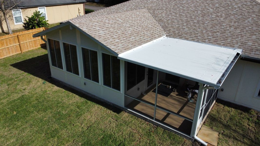White screened-in porch with attached roof, next to a house with brown shingles and a backyard with green grass.