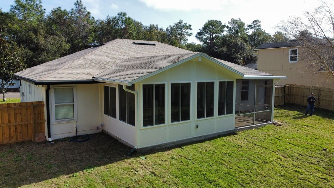 Back view of a white house with a screened-in porch on a grassy yard, surrounded by trees and a fence.