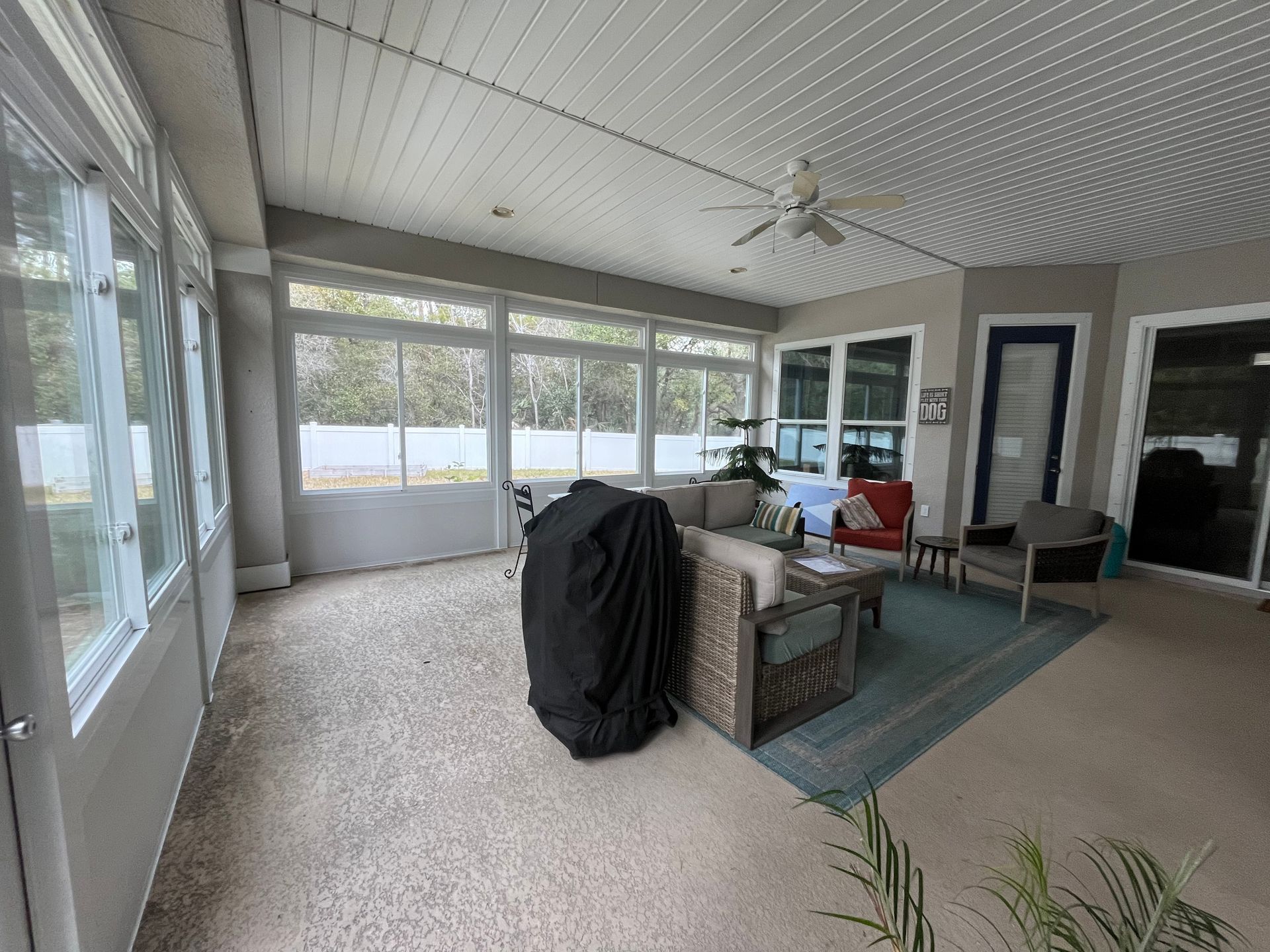 Sunroom with windows, ceiling fan, and outdoor furniture. A grill is covered.