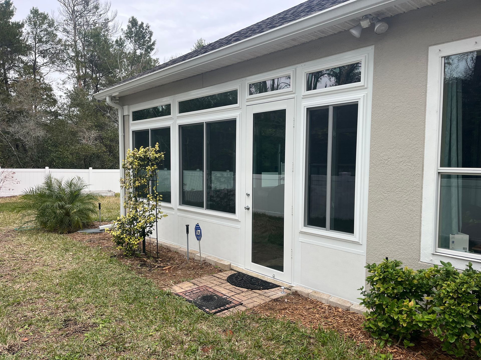 Backyard view of a white-framed sunroom with glass windows and door, located next to grass and a fence.