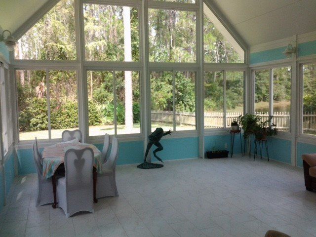 Sunroom with large windows, light blue walls, white chairs, and a frog statue.