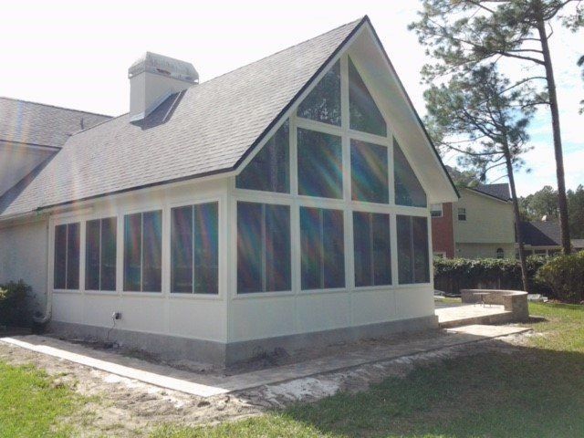 White sunroom addition with screen windows and a black shingle roof, attached to a house with green grass.