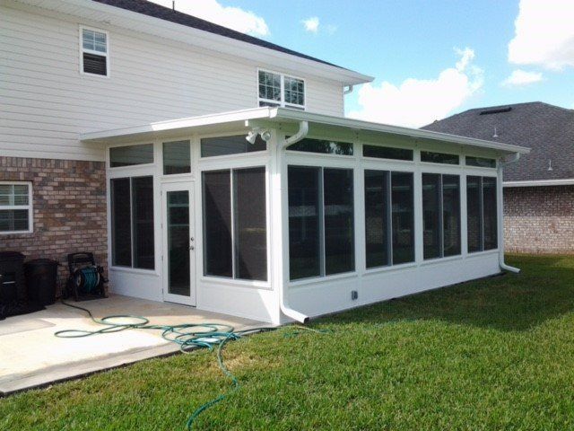 White sunroom attached to a house with screens and windows, on a concrete patio and grass.