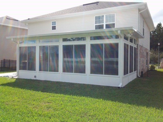 White sunroom addition attached to a two-story beige house; green lawn.