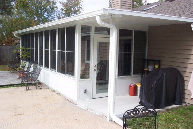 Screened-in porch attached to a house; white frame, concrete patio, glass door, and gutter.