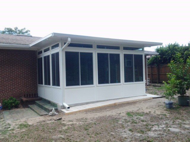 White screened-in porch addition attached to a brick home with concrete base.