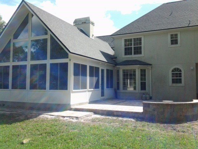 Exterior of a house with a screened-in porch and patio area. White walls, gray roof, and green grass.