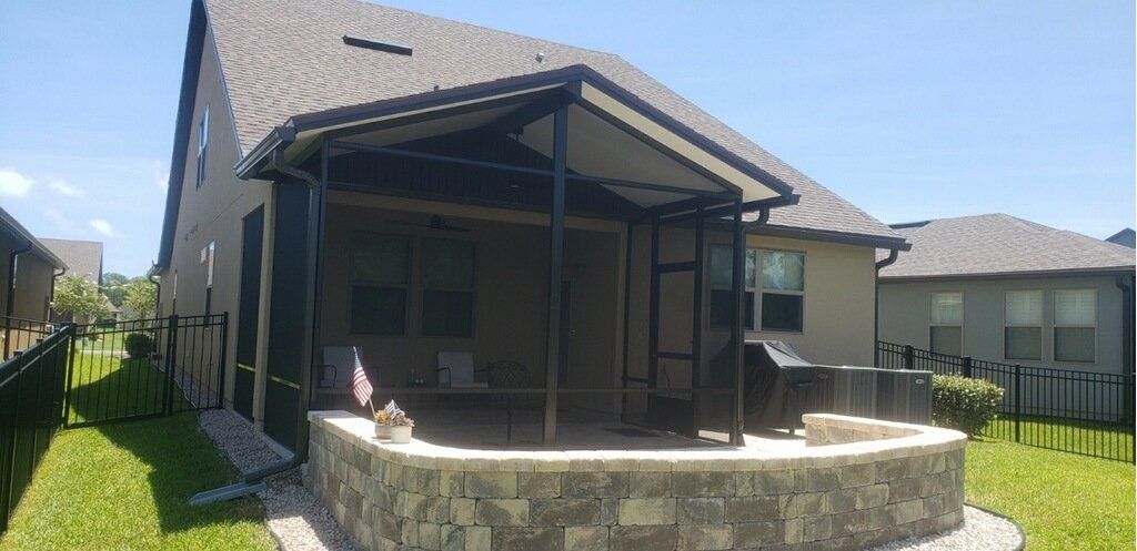 A screened-in patio with a stone retaining wall in front of a house, sunny day.