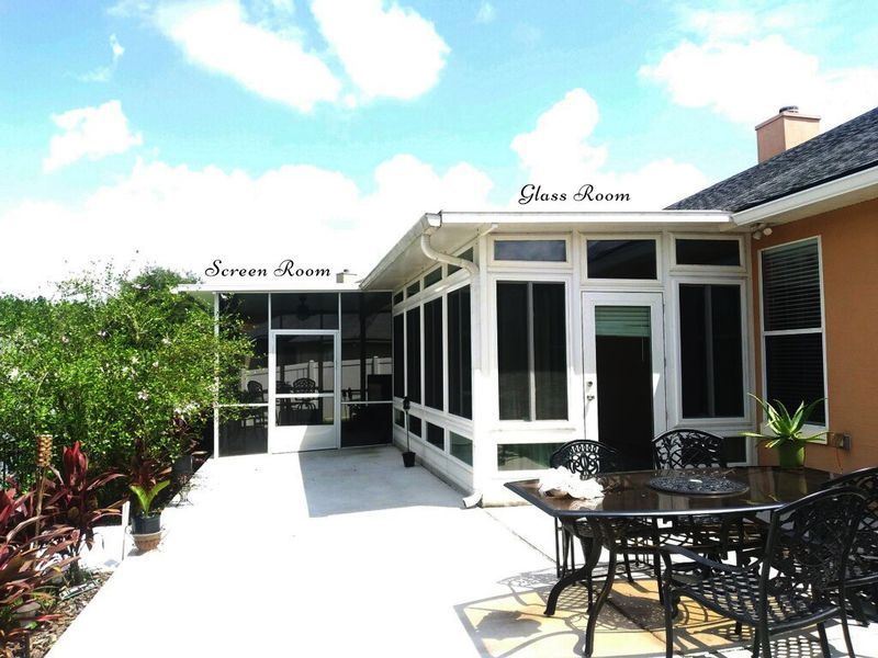 Screen room and glass room addition on a sunny patio, connected to a stucco house.