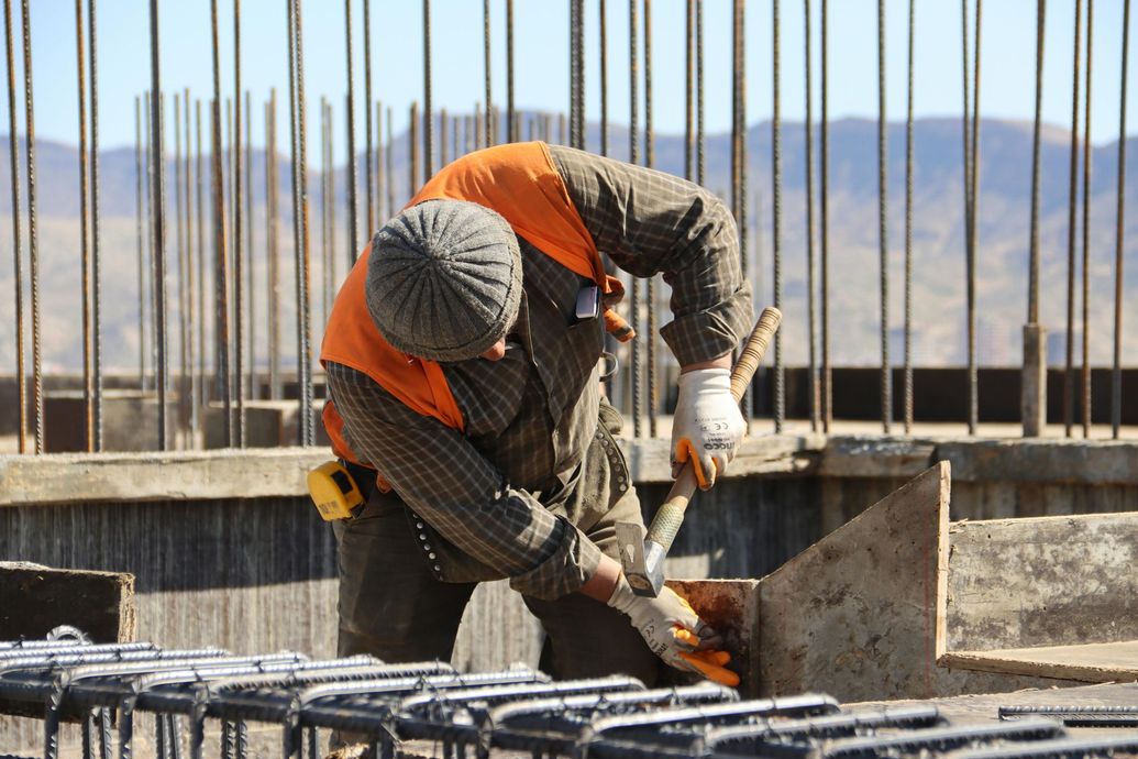 Construction worker bending over rebar, using a power tool on a concrete structure.
