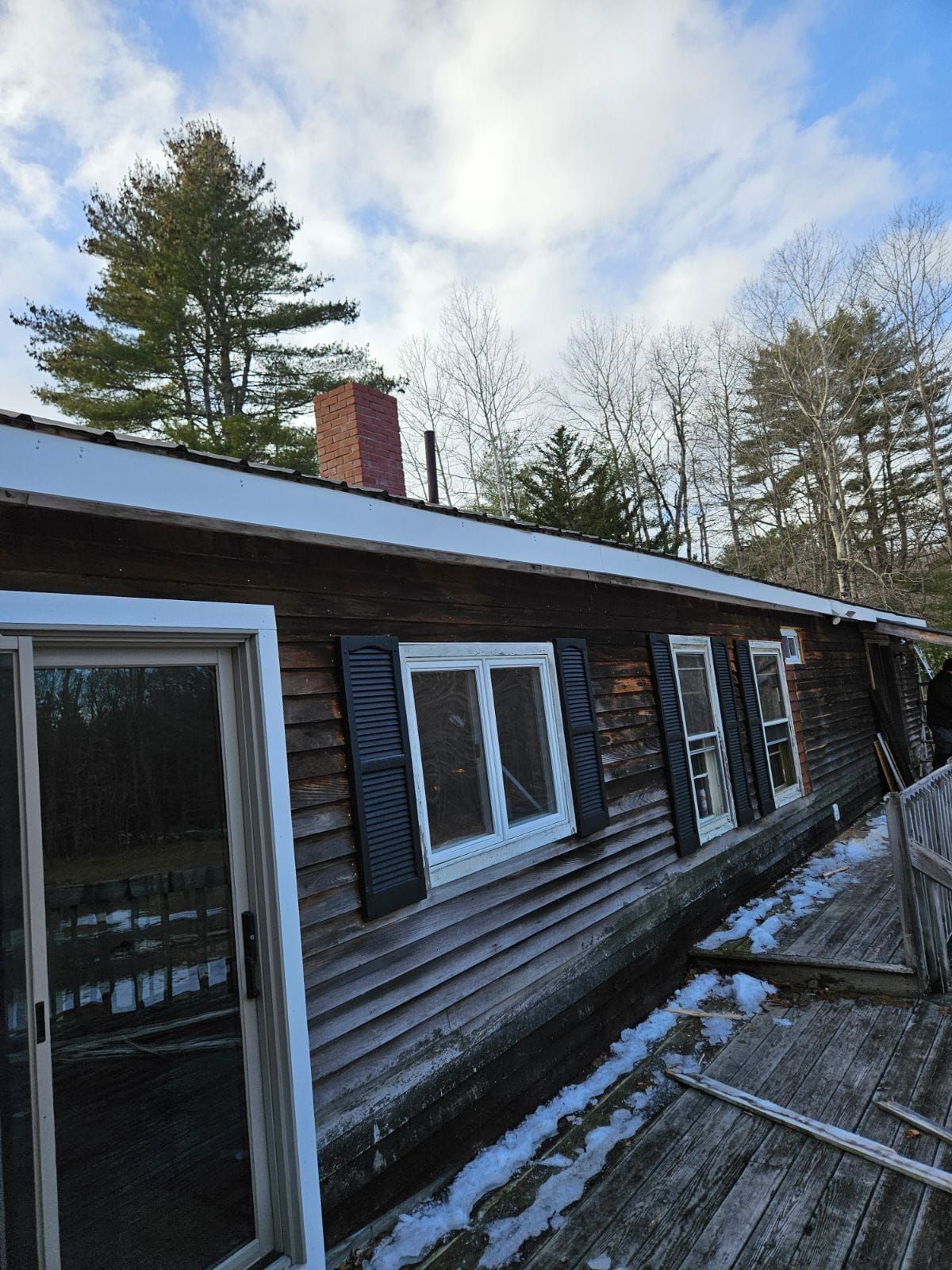 A wooden house with a sliding glass door and black shutters.
