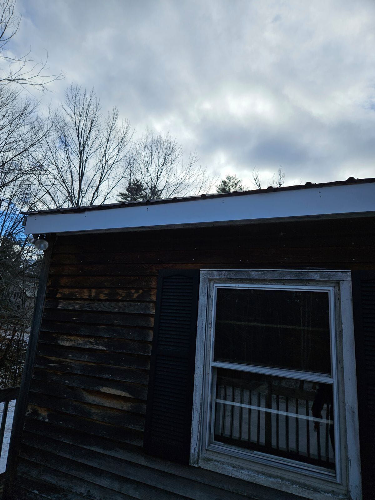 A window on the side of a house with a cloudy sky in the background.