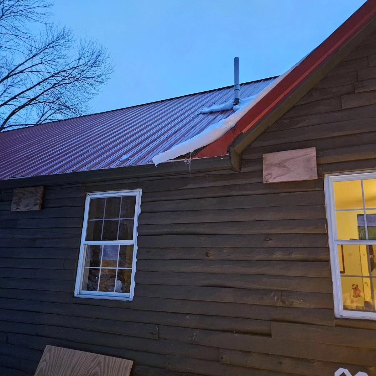 A wooden house with a red roof and two windows