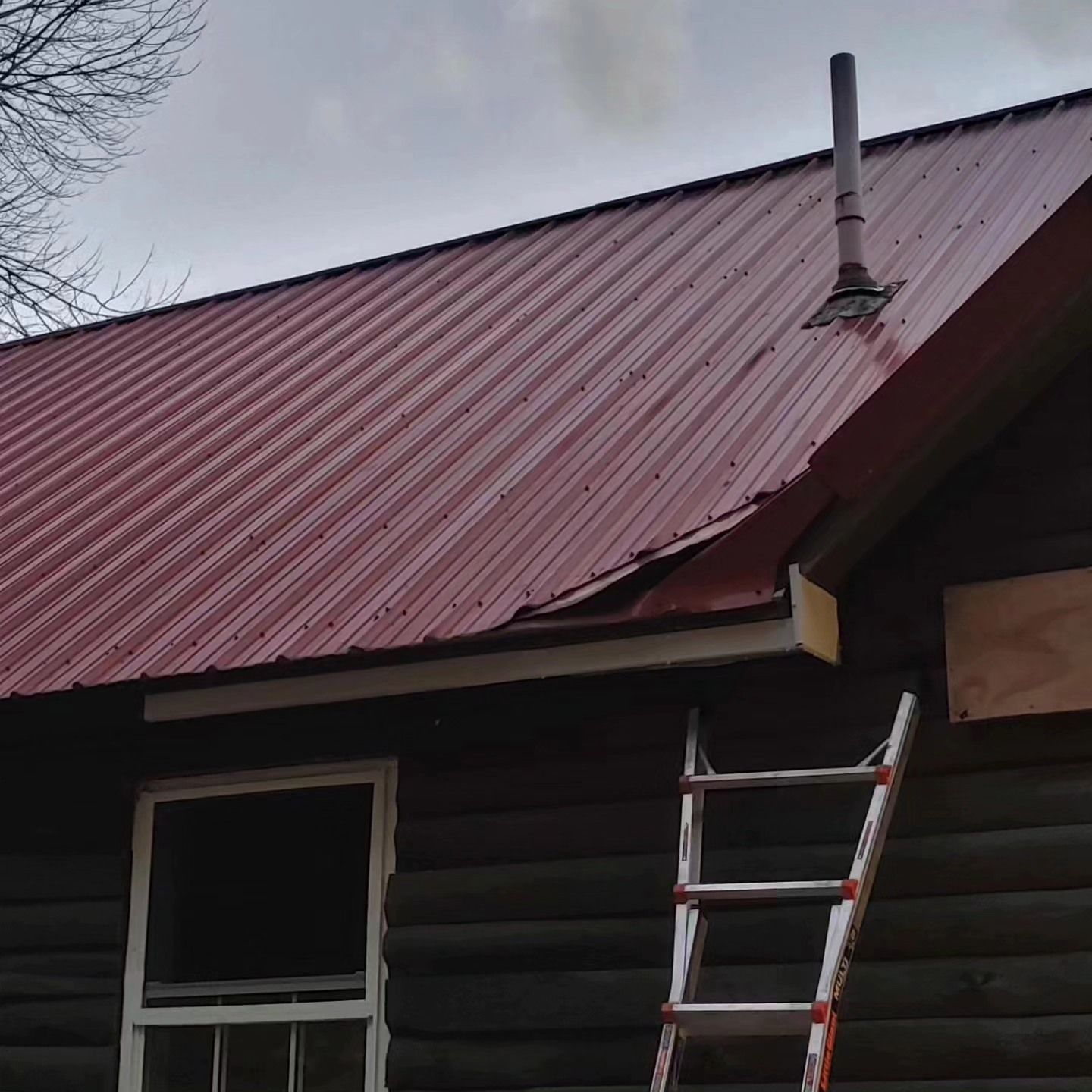 A ladder is sitting on the side of a house with a red roof