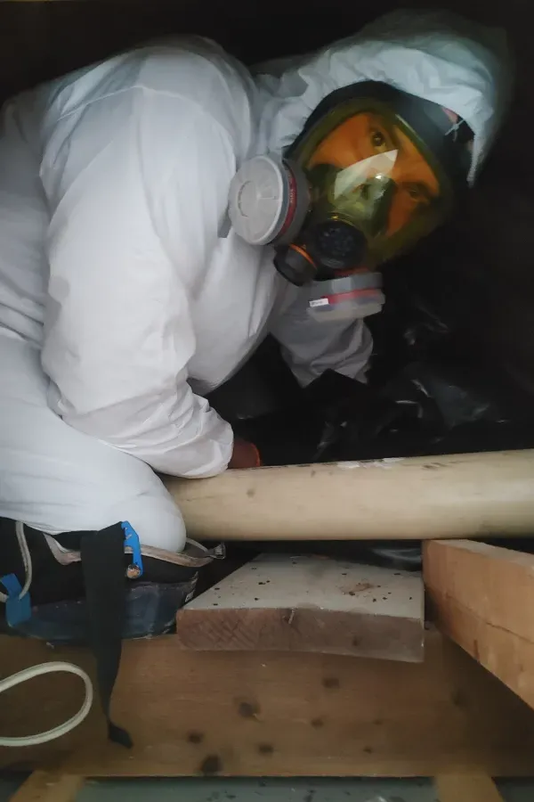 A person wearing a gas mask is crawling under a pipe